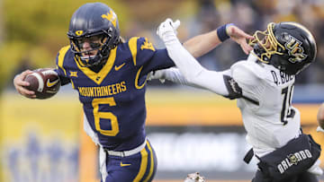 Nov 23, 2024; Morgantown, West Virginia, USA; West Virginia Mountaineers quarterback Garrett Greene (6) stiff arms UCF Knights defensive back Quadric Bullard (10) during the first quarter at Mountaineer Field at Milan Puskar Stadium. Mandatory Credit: Ben Queen-Imagn Images