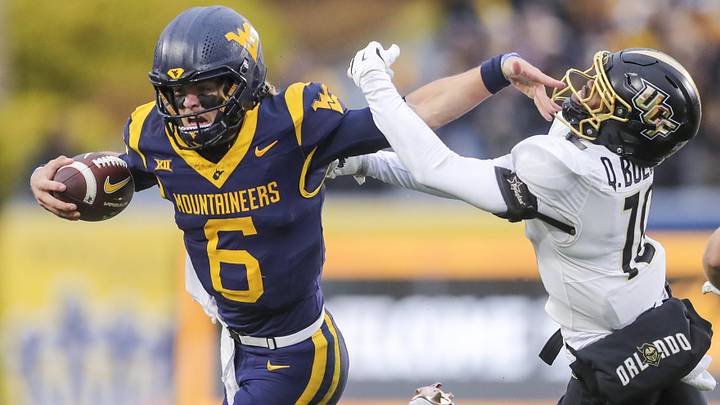 Nov 23, 2024; Morgantown, West Virginia, USA; West Virginia Mountaineers quarterback Garrett Greene (6) stiff arms UCF Knights defensive back Quadric Bullard (10) during the first quarter at Mountaineer Field at Milan Puskar Stadium. Mandatory Credit: Ben Queen-Imagn Images