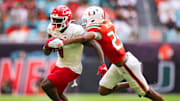 Nov 18, 2023; Miami Gardens, Florida, USA; Louisville Cardinals wide receiver Chris Bell (0) breaks a tackle attempt from Miami Hurricanes defensive back Jadais Richard (25) during the second quarter at Hard Rock Stadium. Mandatory Credit: Sam Navarro-Imagn Images