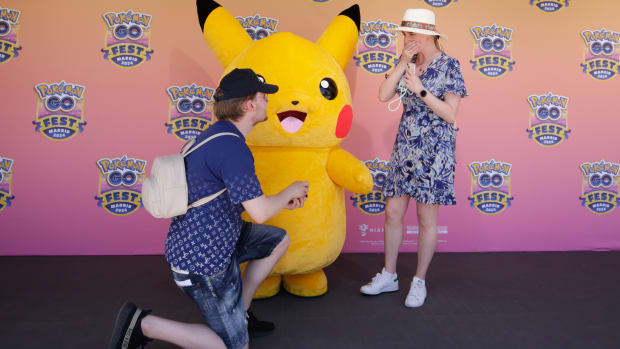 Pikachu standing between two people getting engaged.