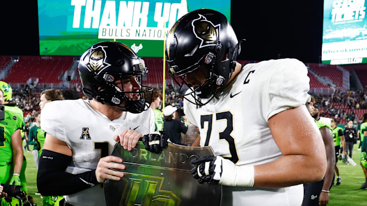 Nov 26, 2022; Tampa, Florida, USA; UCF Knights quarterback John Rhys Plume (10) and offensive lineman Samuel Jackson (73) hold the war on I-4 trophy at midfield following defeating the South Florida Bulls at Raymond James Stadium. Mandatory Credit: Douglas DeFelice-Imagn Images Nov 26, 2022; Tampa, Florida, USA; UCF Knights quarterback John Rhys Plume (10) and offensive lineman Samuel Jackson (73) hold the war on I-4 trophy at midfield following defeating the South Florida Bulls at Raymond James Stadium. Mandatory Credit: Douglas DeFelice-Imagn Images
