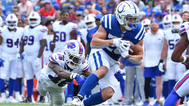 Colts running back Evan Hull (blue jersey with white pants/helmet) runs past a defender (all-white uniform) on the field. 