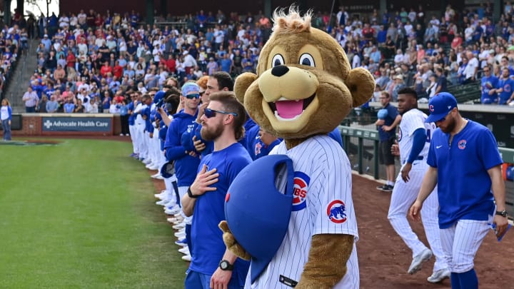 Feb 27, 2024; Mesa, Arizona, USA;  Chicago Cubs mascot Clark and players look on during the national anthem prior to a spring training game against the Cincinnati Reds at Sloan Park.