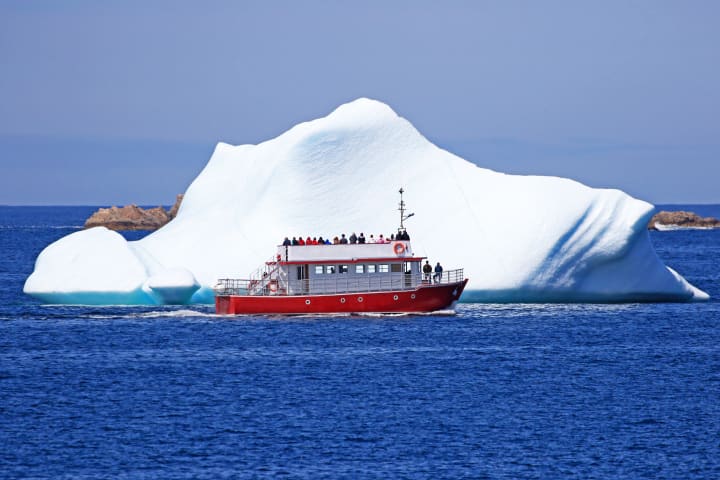 Ein Ausflugsboot, das in der Nähe eines Eisbergs in Neufundland, Kanada, segelt.