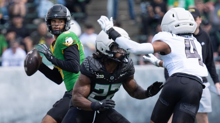 Combat Duck Dante Moore, left, drops back to pass behind a block by Jay Harris against Fighting Duck 
Brandon Finny during the fourth quarter of the Oregon Spring Game.
