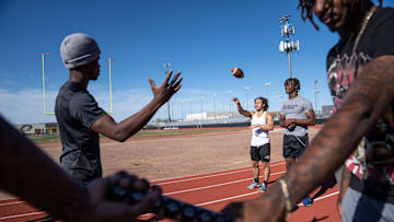 Desert Edge High School athletes Camren Hamiel, left, prepares to catch a pass from Antonio Para, center, as they pose for a portrait with teammates on campus in Goodyear on March 29, 2024.