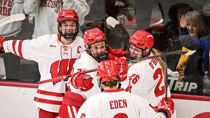 Teammates mob Wisconsin Badgers left wing Kirsten Simms (27) after her goal against the Minnesota Gophers in the second period of a game Sunday, February 9, 2025, at LaBahn Arena in Madison, Wisconsin.