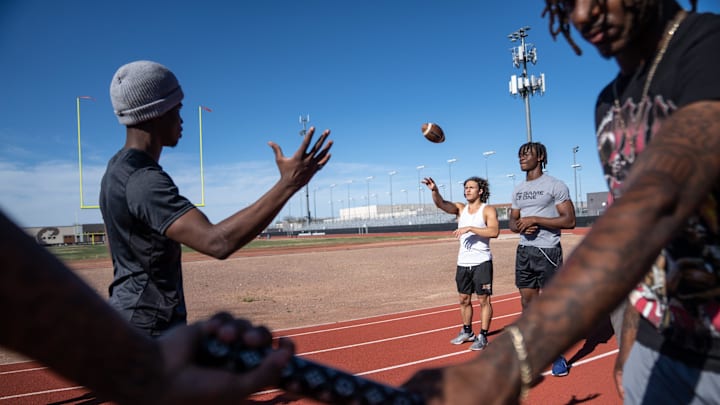 Desert Edge High School athletes Camren Hamiel, left, prepares to catch a pass from Antonio Para, center, as they pose for a portrait with teammates on campus in Goodyear on March 29, 2024.