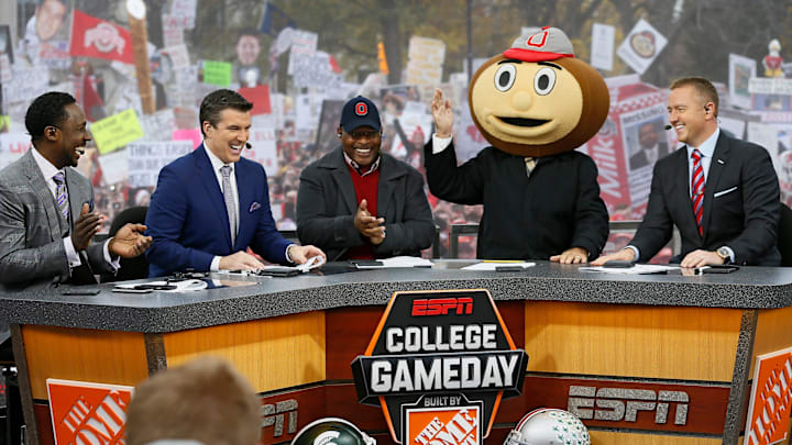 Lee Corso waves while wearing a Brutus Buckeye head as, from left, Desmond Howard, Rece Davis, Archie Griffin, and Kirk Herbstreit applaud his pick during ESPN's College GameDay broadcast from the campus of Ohio State prior to the NCAA football game against the Michigan State Spartans in Columbus on Nov. 21, 2015.