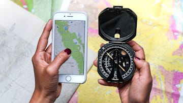 Hand holding map on phone in front of paper maps