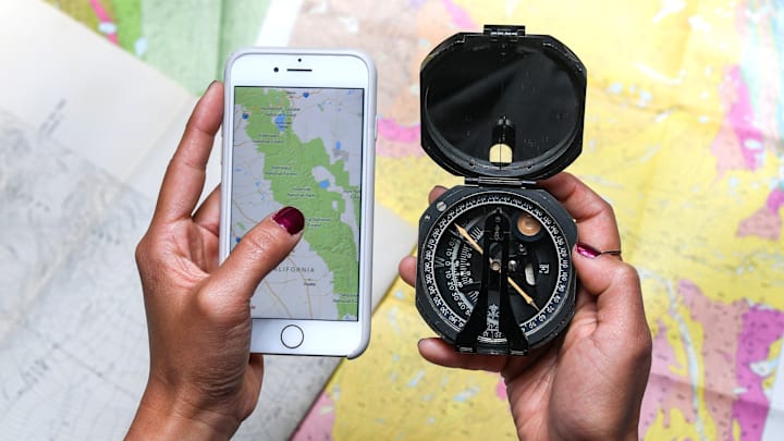 Hand holding map on phone in front of paper maps