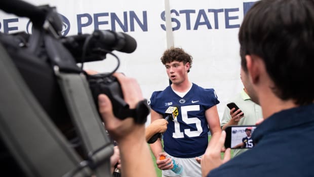 Penn State quarterback Drew Allar answers a question in front of a television cameraman and with reporters around him.