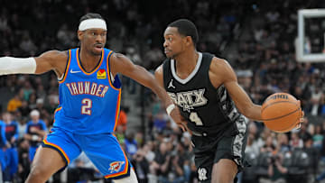 Mar 2, 2025; San Antonio, Texas, USA;  San Antonio Spurs guard De'Aaron Fox (4) dribbles against Oklahoma City Thunder guard Shai Gilgeous-Alexander (2) in the first half at Frost Bank Center. Mandatory Credit: Daniel Dunn-Imagn Images