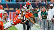 Nov 8, 2025; Miami Gardens, Florida, USA; Syracuse Orange quarterback Rickie Collins (10) leaps to avoid the tackle of Miami Hurricanes safety Zechariah Poyser (7) during the second quarter at Hard Rock Stadium. Mandatory Credit: Jeff Romance-Imagn Images