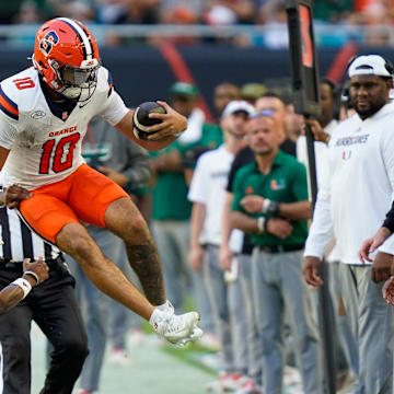Nov 8, 2025; Miami Gardens, Florida, USA; Syracuse Orange quarterback Rickie Collins (10) leaps to avoid the tackle of Miami Hurricanes safety Zechariah Poyser (7) during the second quarter at Hard Rock Stadium. Mandatory Credit: Jeff Romance-Imagn Images