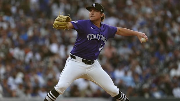 Colorado Rockies reliever Ryan Rolison throws a pitch off the mound, wearing a purple jersey and a black hat.
