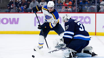 Dec 3, 2024; Winnipeg, Manitoba, CAN;  St. Louis Blues forward Radek Faksa (12) looks for the puck in front of Winnipeg Jets goalie Connor Hellebuyck (37) during the first period at Canada Life Centre. Mandatory Credit: Terrence Lee-Imagn Images