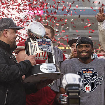 Head coach Matt Rhule holds the Pinstripe Bowl trophy as Nebraska players celebrate their win over Boston College.