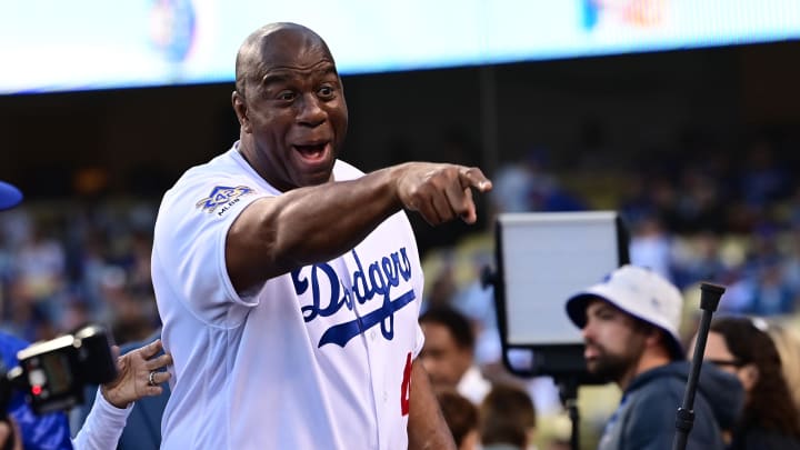 Apr 15, 2022; Los Angeles, California, USA; Magic Johnson points to players in the dugout as he was on had for pre-game ceremonies to celebrate the 75th anniversary of Jackie Robinson breaking the color barrier in Major League Baseball before the game between the Los Angeles Dodgers and the Cincinnati Reds at Dodger Stadium. Mandatory Credit: Jayne Kamin-Oncea-USA TODAY Sports