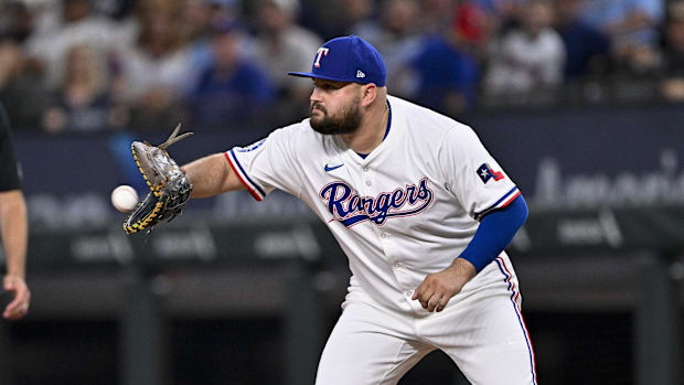 Texas Rangers first baseman Rowdy Tellez catches a baseball while wearing a white uniform and blue hat