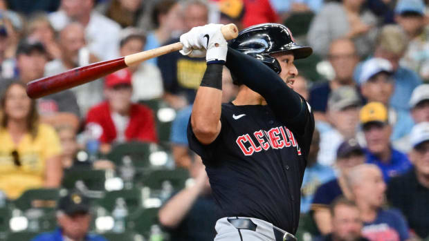 A baseball player wearing a navy jersey, gray pants, and a navy helmet while swinging a baseball bat.