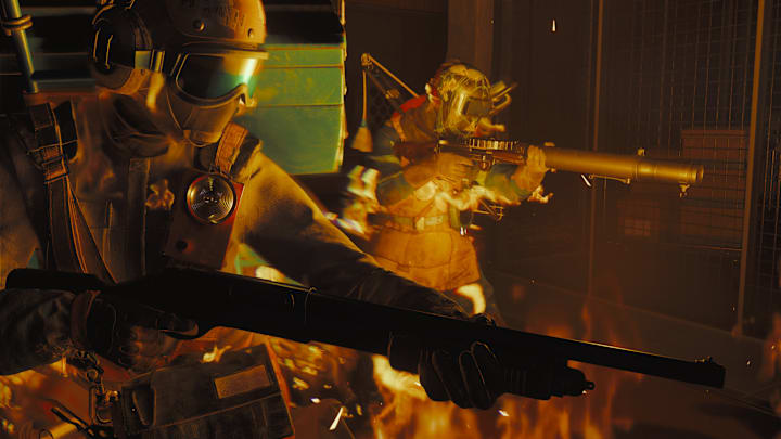 Two people in military gear holding shotguns walking through fire.