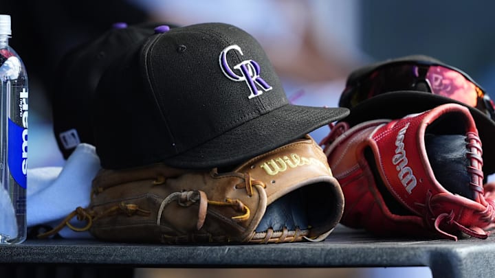 A Colorado Rockies hat sits on top of a player's glove in a dugout. 
