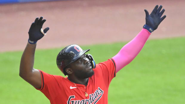 A baseball player wearing a red jersey and navy batting helmet with his arms raised in the air.