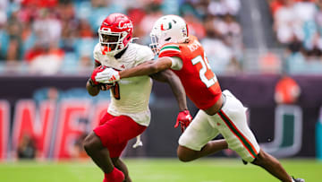 Nov 18, 2023; Miami Gardens, Florida, USA; Louisville Cardinals wide receiver Chris Bell (0) breaks a tackle attempt from Miami Hurricanes defensive back Jadais Richard (25) during the second quarter at Hard Rock Stadium. Mandatory Credit: Sam Navarro-Imagn Images