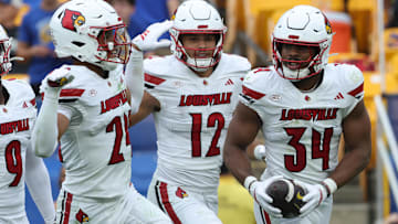 Sep 27, 2025; Pittsburgh, Pennsylvania, USA;  Louisville Cardinals defensive back Corey Gordon (24) and linebacker Kalib Perry (12) celebrate an interception by linebacker TJ Quinn (34) against the Pittsburgh Panthers during the fourth quarter at Acrisure Stadium. Mandatory Credit: Charles LeClaire-Imagn Images