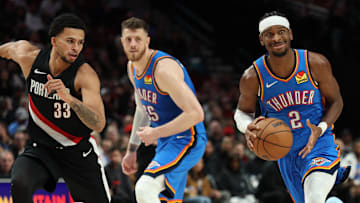 Nov 5, 2025; Portland, Oregon, USA;  Oklahoma City Thunder guard Shai Gilgeous-Alexander (2) dribbles the ball past Portland Trail Blazers forward Toumani Camara (33) as teammate Thunder’s center/forward Isaiah Hartenstein (55) watches during the first half at Moda Center. Mandatory Credit: Jaime Valdez-Imagn Images

