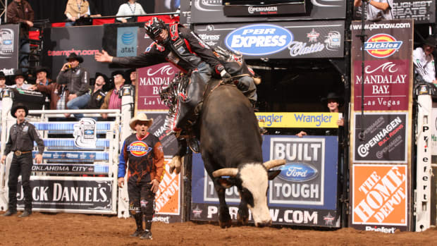 A bull rider attempting to ride a black bucking bull by the name of Bones.