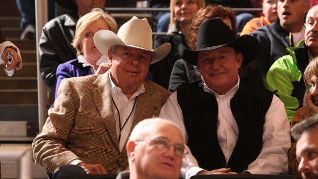 Two cowboys sitting beside each other in the grandstands watching a bull riding.