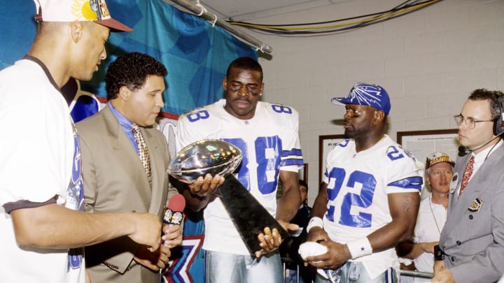 Jan 28, 1996; Tempe, AZ; USA; FILE PHOTO; NBC sportscaster Greg Gumble and Dallas Cowboys running back Emmitt Smith (22) and cornerback Larry Brown (left) look on as wide receiver Michael Irvin (88) holds the Lombardi trophy after defeating the Pittsburgh Steelers 27-17 in Super Bowl XXX at Sun Devil Stadium. 