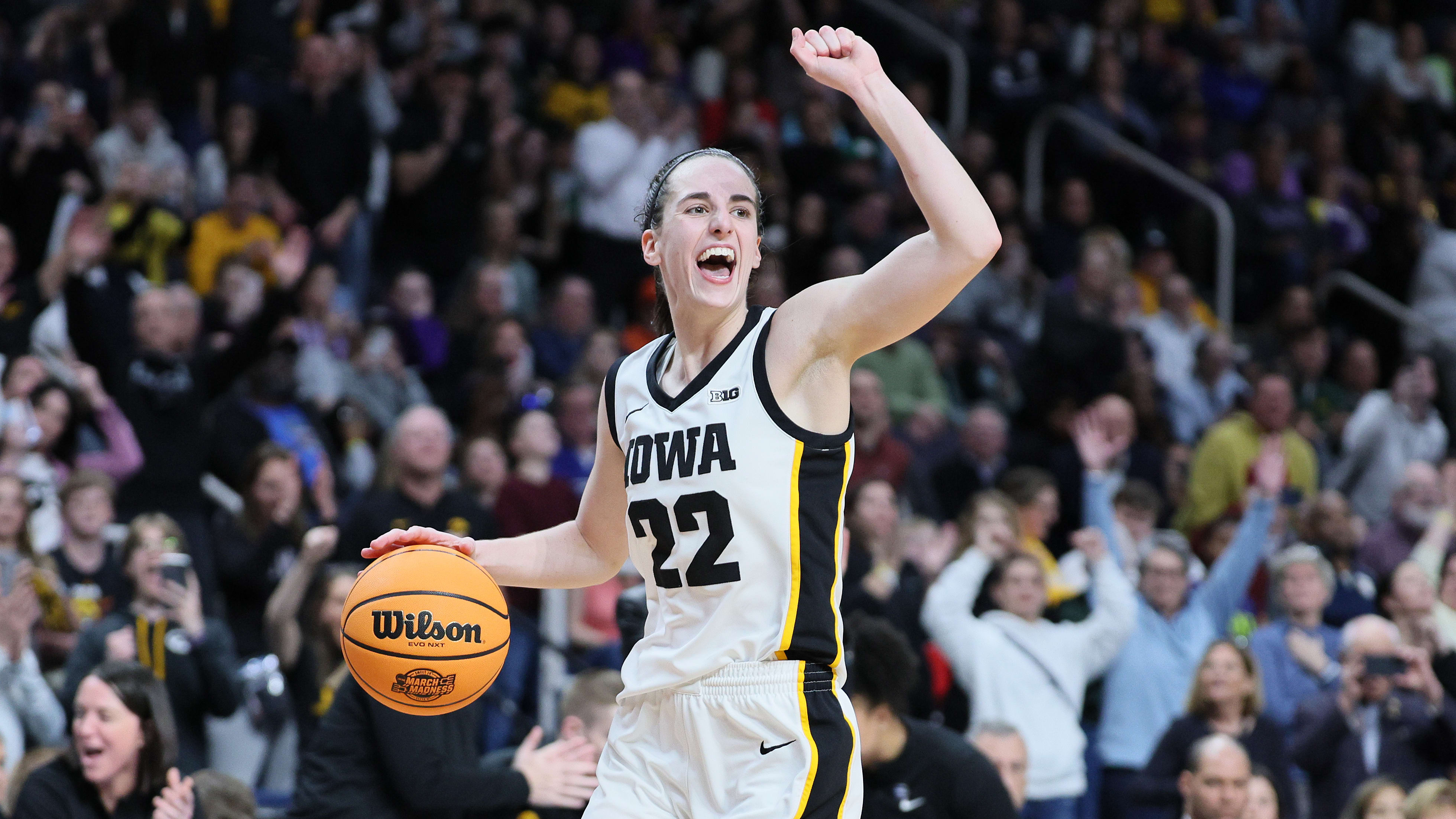Caitlin Clark celebrates by pumping her left fist into the air while dribbling a basketball