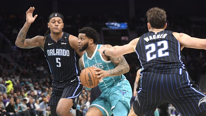 Mar 25, 2025; Charlotte, North Carolina, USA;  Charlotte Hornets forward Miles Bridges (0) drives past Orlando Magic forward Paolo Banchero (5) and forward Franz Wagner (22) during the second half at the Spectrum Center. Mandatory Credit: Sam Sharpe-Imagn Images