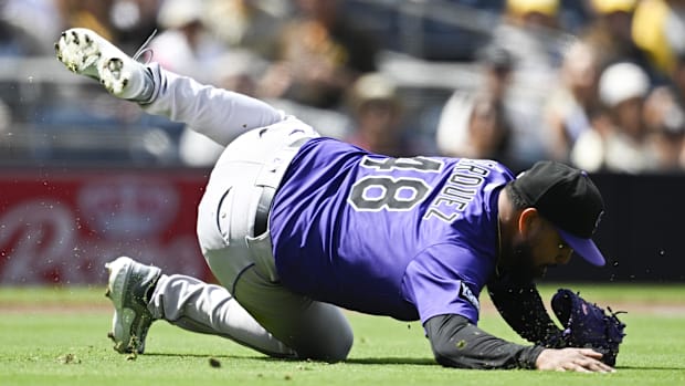 Colorado Rockies pitcher German Marquez fields a ball on the ground wearing a purple jersey and black and purple hat.