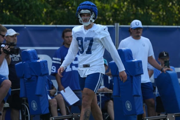 Football player Laiatu Latu walks across the filed at training camp in a white jersey.