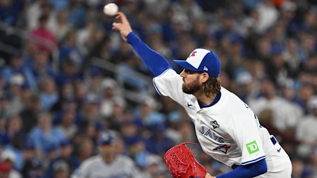 Toronto Blue Jays pitcher Kevin Gausman throws a pitch, wearing a white jersey and a white and blue hat.  Toronto Blue Jays pitcher Kevin Gausman throws a pitch, wearing a white jersey and a white and blue hat.