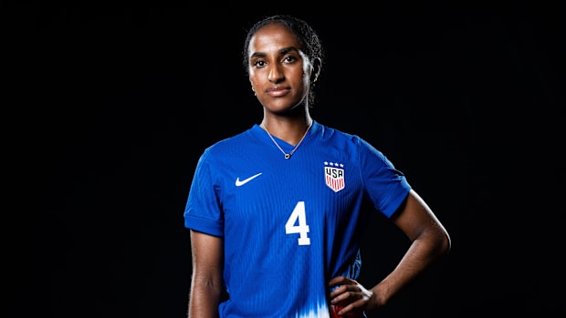 Naomi Girma's poses for a photo in a studio wearing her USA soccer team uniform.