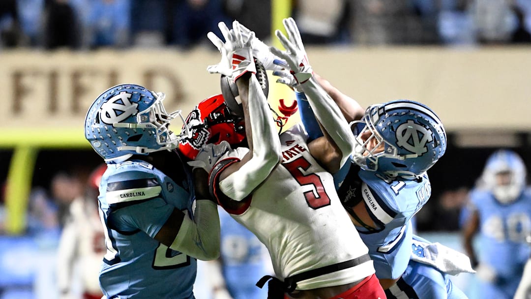 Nov 30, 2024; Chapel Hill, North Carolina, USA; North Carolina State Wolfpack wide receiver Noah Rogers (5) catches a 44 yard pass as North Carolina Tar Heels defensive back Marcus Allen (29) and North Carolina Tar Heels defensive back Will Hardy (31) defend in the fourth quarter at Kenan Memorial Stadium. Mandatory Credit: Bob Donnan-Imagn Images