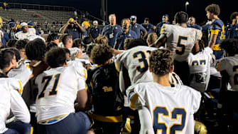 St. Thomas Aquinas coach Roger Harriott addresses team after the Raiders rallied past Western, 23-15, on a rainy night.