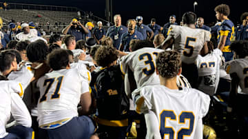 St. Thomas Aquinas coach Roger Harriott addresses team after the Raiders rallied past Western, 23-15, on a rainy night.