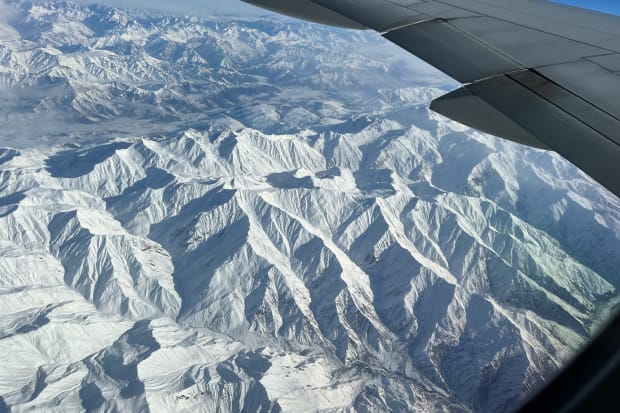 Looking out an airplane window seeing snow covered mountain tops in the Himalayas.