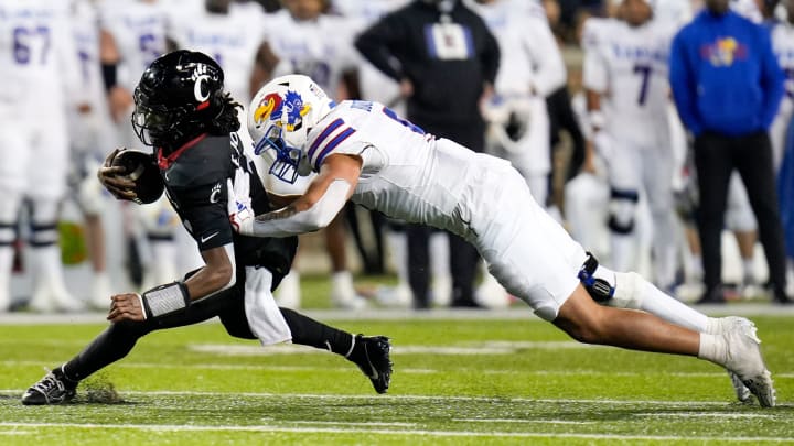 Cincinnati Bearcats quarterback Emory Jones (5) drives the ball as Kansas Jayhawks defensive lineman Austin Booker (9) tackles him to the ground during the NCAA college football game between the Cincinnati Bearcats and Kansas Jayhawks on Saturday, Nov. 25, 2023, at Nippert Stadium in Cincinnati. Kansas won 49-16.