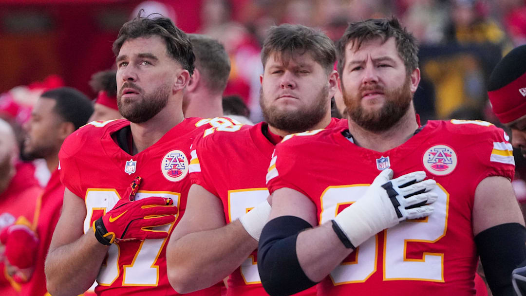 Nov 29, 2024; Kansas City, Missouri, USA; Kansas City Chiefs tight end Travis Kelce (87) and center Creed Humphrey (52) and guard Joe Thuney (62) stand for the national anthem prior to a game against the Las Vegas Raiders at GEHA Field at Arrowhead Stadium. Mandatory Credit: Denny Medley-Imagn Images