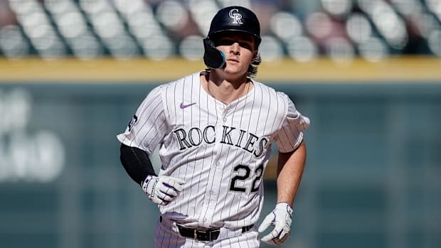 Colorado Rockies center fielder Mickey Moniak runs in a white uniform with purple pinstripes and a black helmet