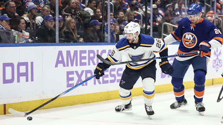 Nov 23, 2024; Elmont, New York, USA;  St. Louis Blues left wing Nathan Walker (26) and New York Islanders defenseman Scott Mayfield (24) chase the puck in the third period at UBS Arena. Mandatory Credit: Wendell Cruz-Imagn Images