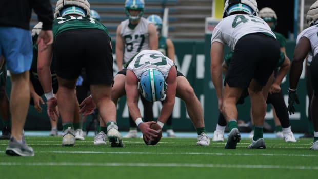 A football player a white jersey with green number and a blue helmet prepares to snap the ball.