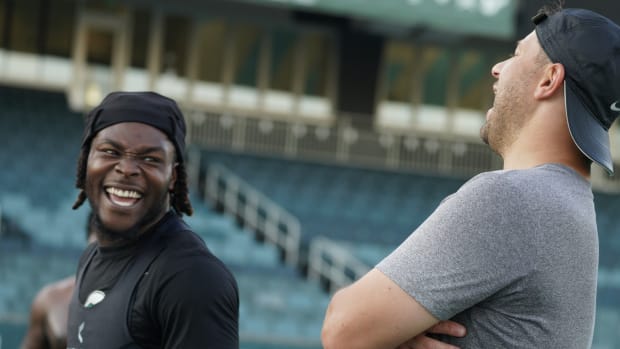 A coach wearing a black hat and grey shirt laughs with a player in a black jersey.